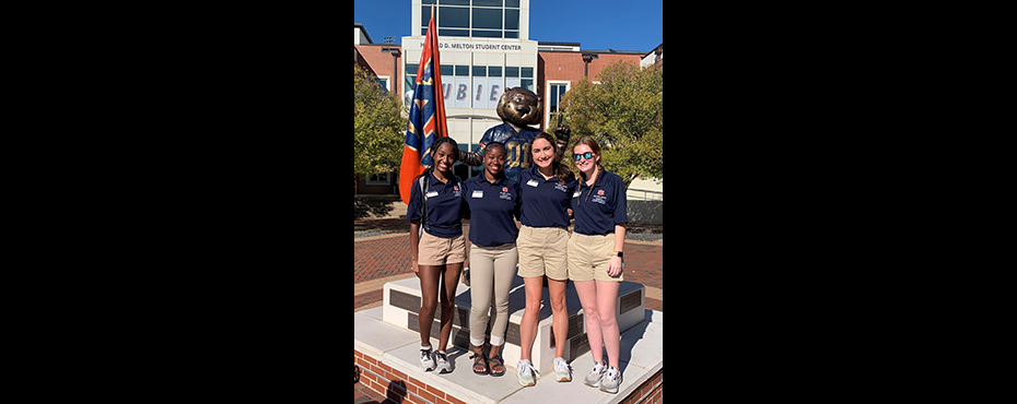 4 female outreach ambassador students stand for a picture outside with the Aubie statue