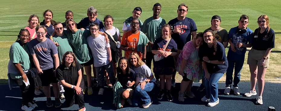 A large group of male and female students and adults stand for a picture with the football field in the background