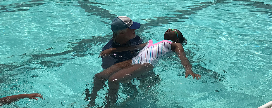 Swim instructors holds girl up in swimming pool to teach her how to float