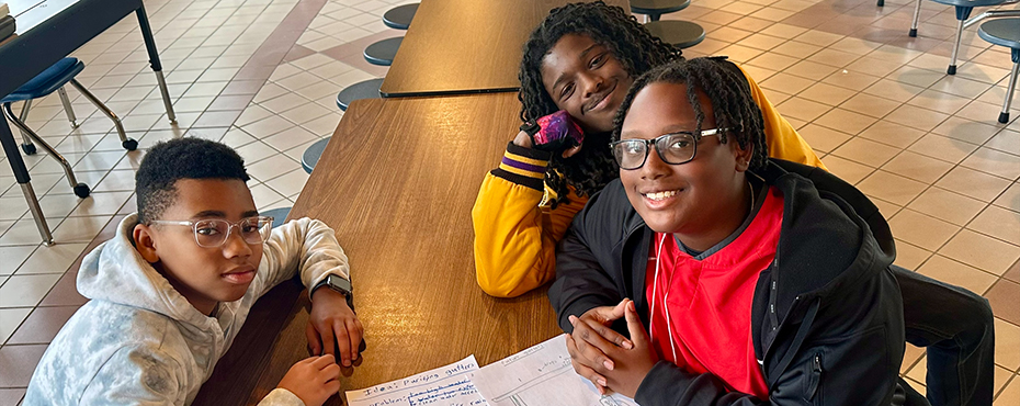 A small group of students work on a group project at a cafeteria table