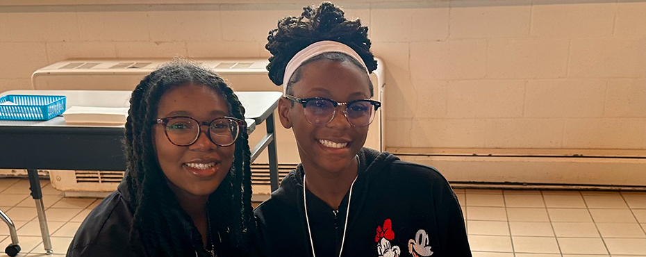 2 female students smile for a picture at a table in a cafeteria area