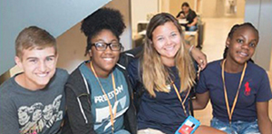 One male and three female students pose and smile for photo while sitting down