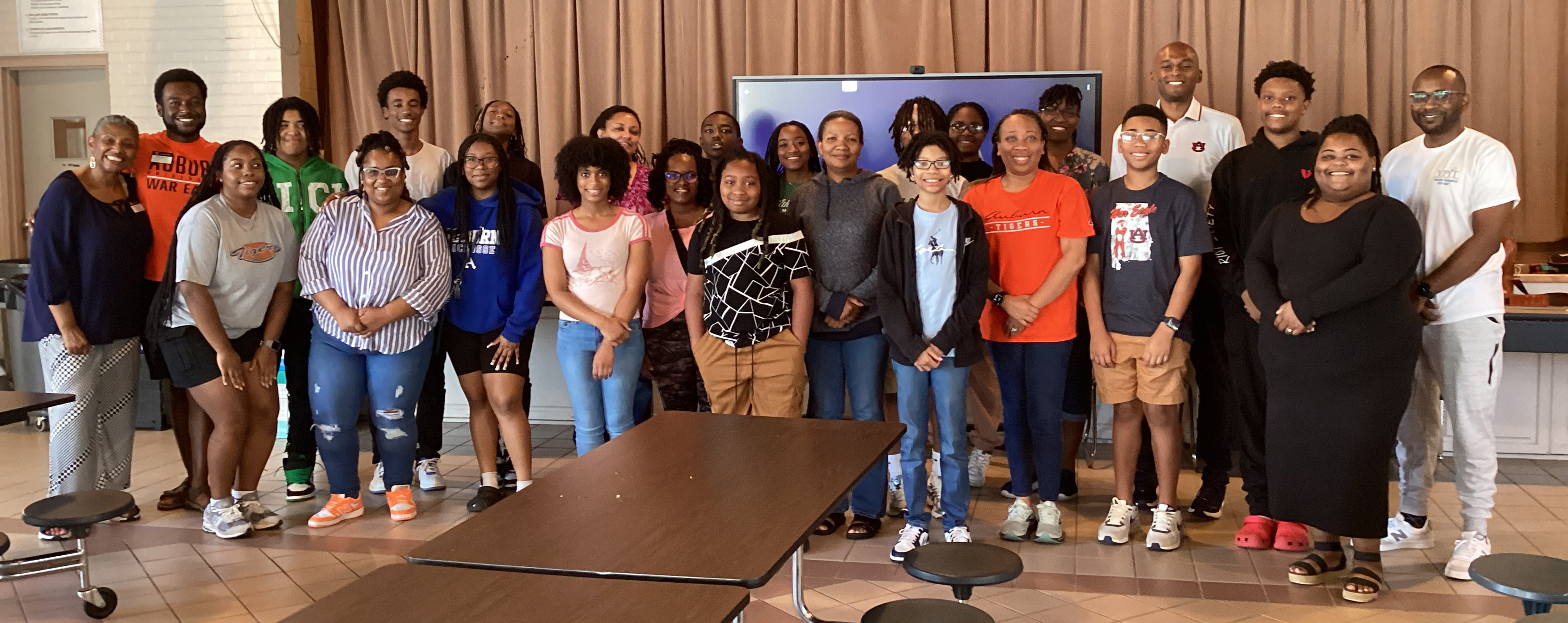 A large group of male and female students and adults stand for a group picture in a community center