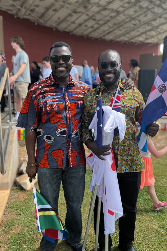 two males attending event in cultural attire and holding flags