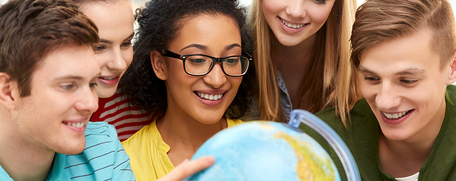 Young students huddled together looking at globe and smiling