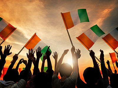 Silhouette of hands with Ireland's flag in background with sunset.