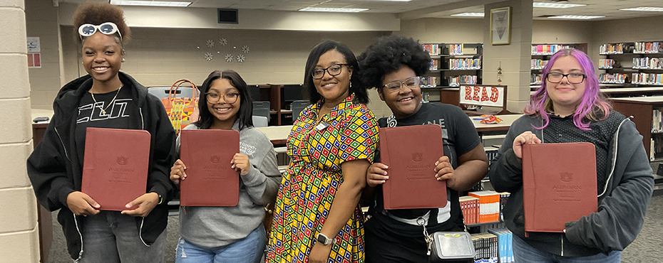 Four girls hold brown padfolios with a woman in the middle