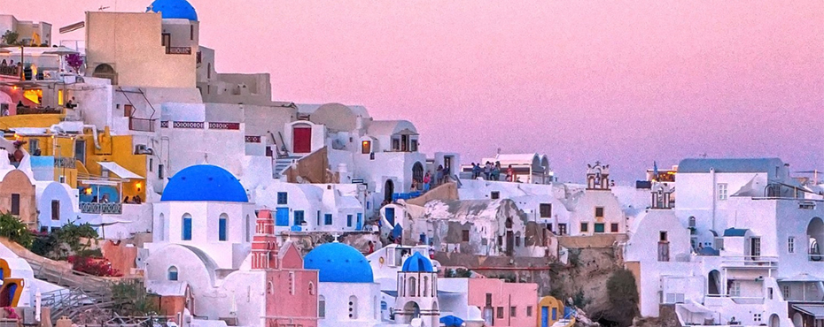 Buildings packed in on the side of a mountain with a pink/purple colored sky 