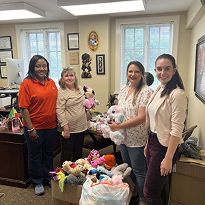 Four women pose with donated stuffed animals and medicines.