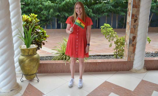 Abby wearing red dress and holding small ghanian flag.