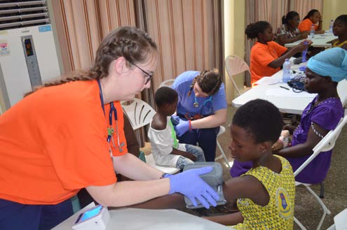 Shelby puts the blood pressure cuff on a small ghanian child during health clinic.