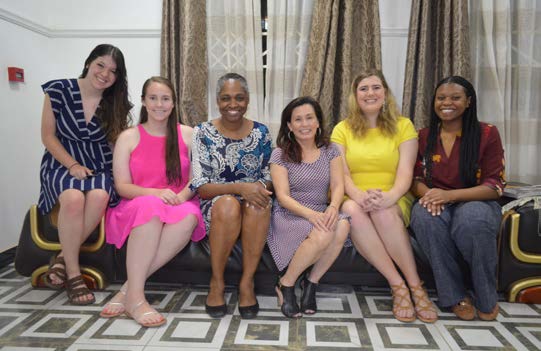 Six women sit on couch and pose for photo.