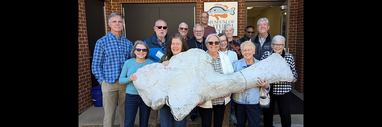 OLLI members work together to hold a large fossil bone outside the Auburn University Museum of Natural History.