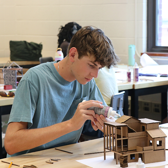 Male student glueing a wooden model house.