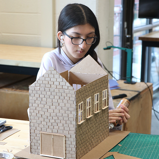 Female student building a cardboard model of a house.