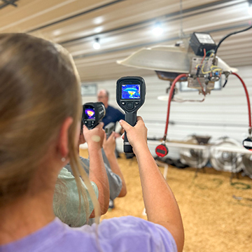 Campers holding heat guns inside a poultry house.