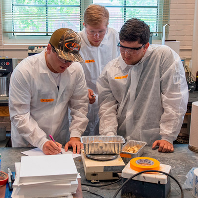 Three male students taking weight measurements of test samples