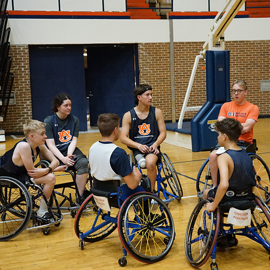 Group of students in wheelchairs in a circle on a basketball court