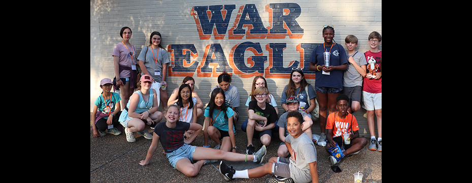 Group of students posing around a WAR EAGLE sign.