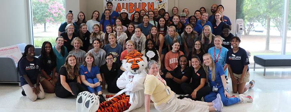 Large group of students with Aubie and an instructor sitting on the floor in front of the group