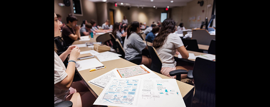 Students in a classroom with design sketches on a desk