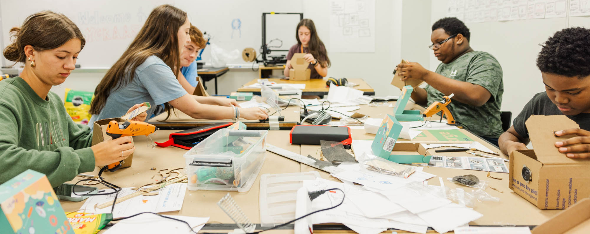 Students sitting around a work table using hot glue guns