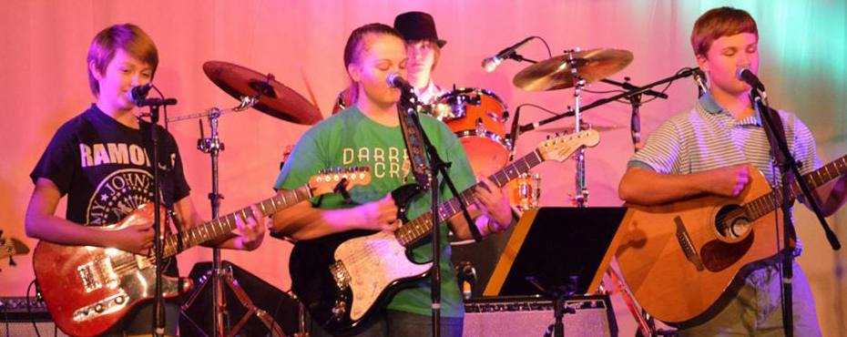 A group of three guitar players gather together to perform on stage at Spicer’s Rock Camp Pro.
