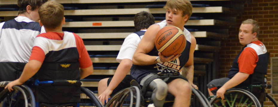 Wheelchair basketball camper shields the ball while scrimmaging at camp.