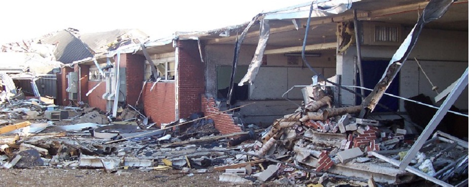 School wing destroyed by Tornado: roof gone and brick wall collapsed. Interior room fully exposed.