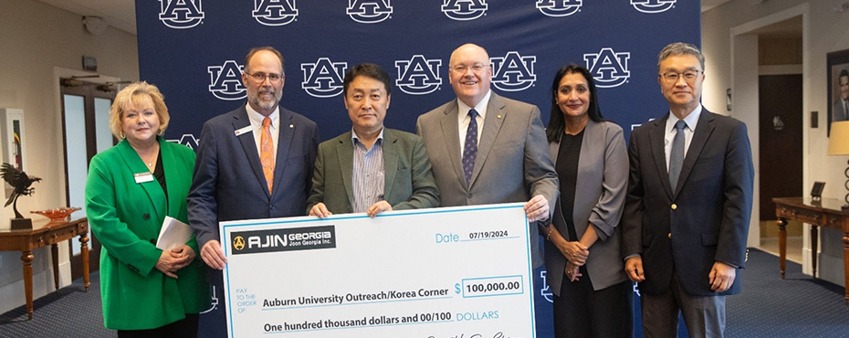 Four men and two women facing camera holding on oversized check representing a donation