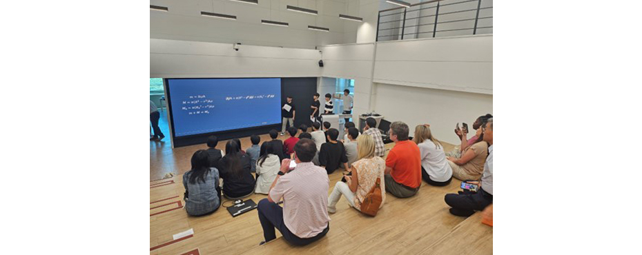 Group photo shot from behind with partipants viewing screen in classroom while sitting on open classroom benches