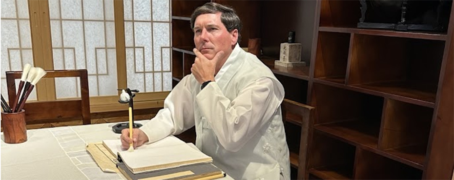 Man sitting at table with book and pen looking upward wearing a white coat