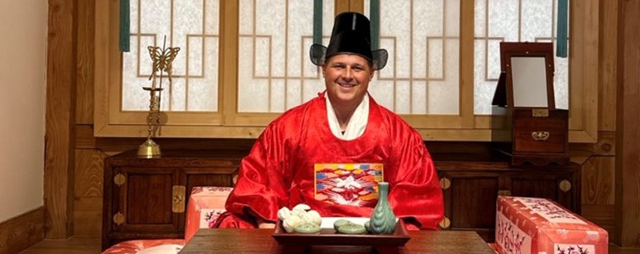 Man facing table in tradtional Korean outfit.